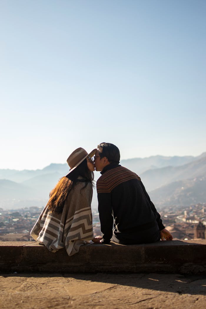 Couple sharing a kiss while sitting on a wall overlooking Cusco, Perú.