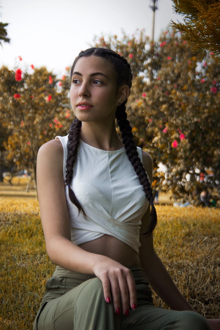 Portrait of a young woman with braided hair, sitting in a park, enjoying the outdoors.